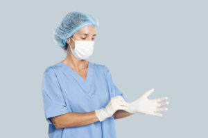 Female plastic surgeon wearing a blue scrub suit, face mask, and hair cap while putting on sterile gloves before a procedure. Dr. Tracy Pfeifer – New York, Hamptons.
