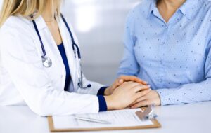 Woman Doctor with Woman Patient talking at a desk, doctor holding patient's hand - Dr Tracy Pfeifer - New York City and The Hamptons